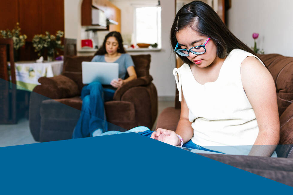 A teenager using a tablet at home and an adult in the background using a computer